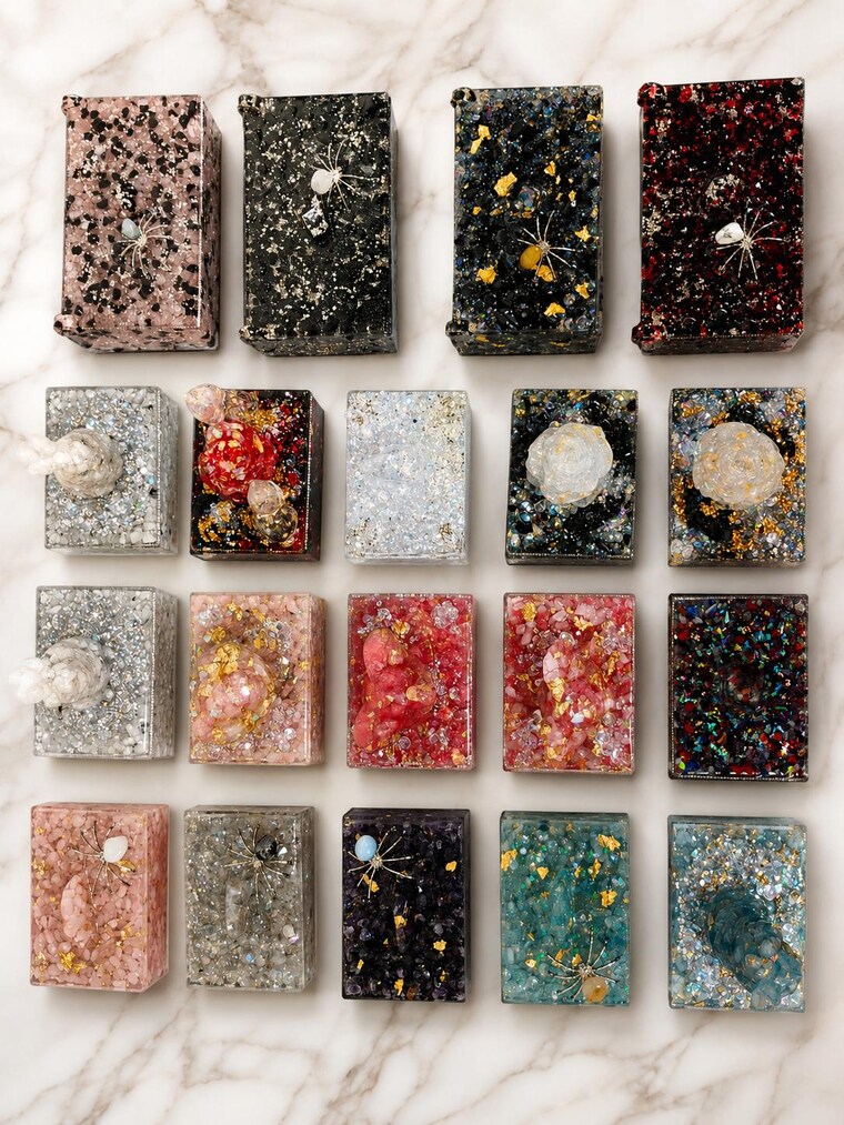 Nineteen finished keepsake boxes laid out together on marble, every one a different colour and arrangement.